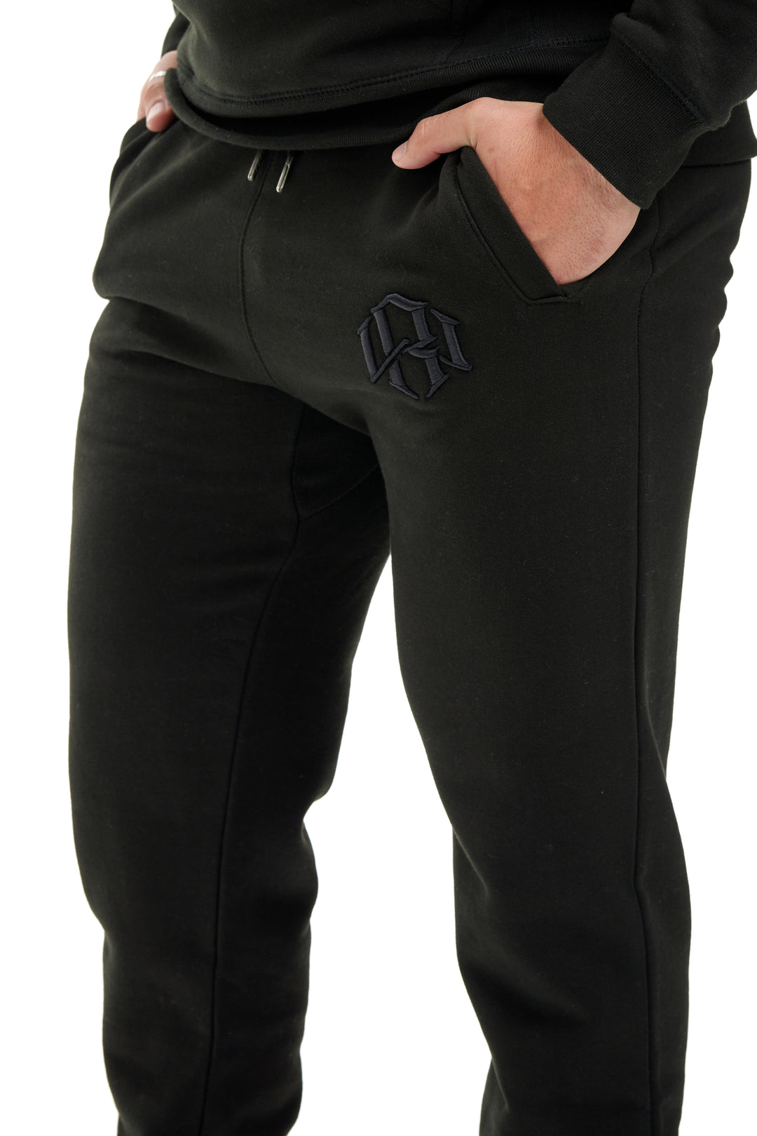 Model wearing Black Sweatpants by RENOWNED WEAR brand with hands in the pockets.