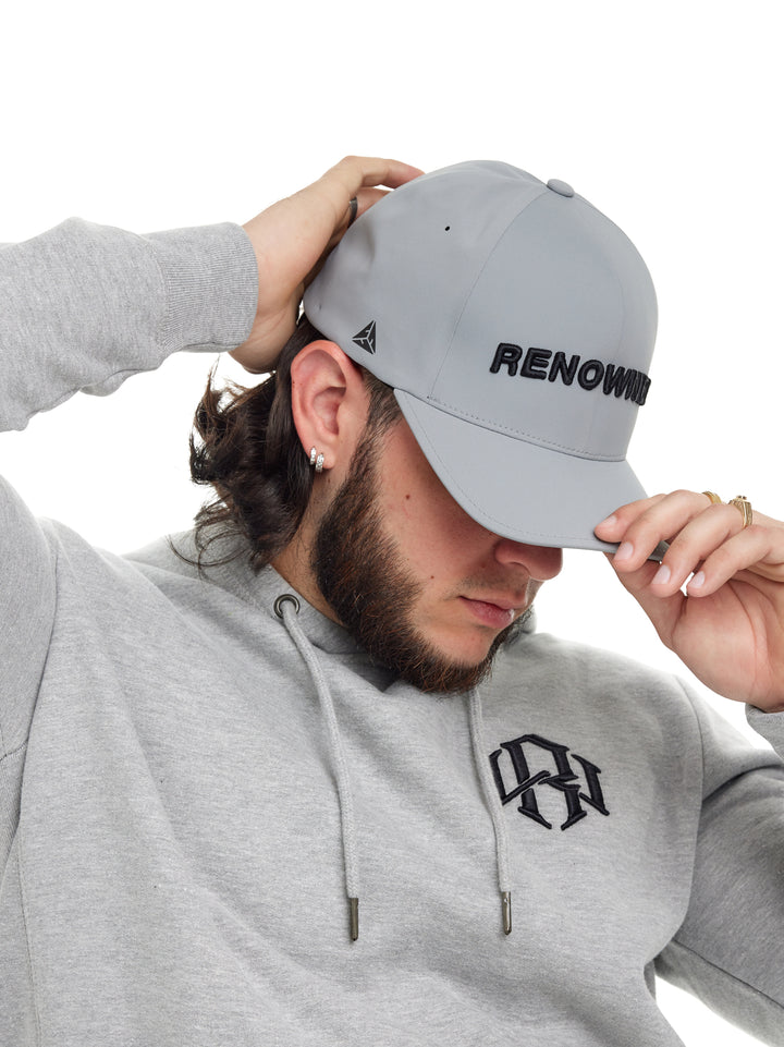 Young man puts on his Renowned Wear Core Silver Baseball Cap with a front 3D Embroidery Brand Name
